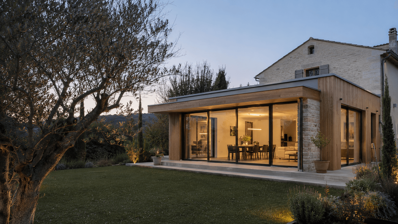 Extension contemporaine en bois d'une longère, terrasse et jardin au crépuscule